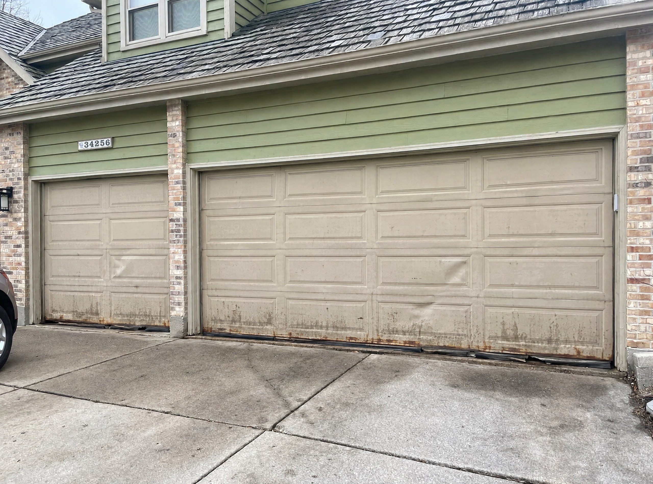 Before: faded, dented almond steel garage doors with rusted bottoms